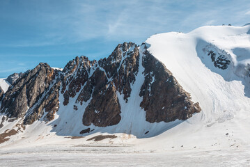 Scenic mountain landscape with glacier under sharp rocks in sunlight. Awesome alpine landscape with glacial tongue in sunshine. Beautiful view to snow mountain tops at very high altitude in sunny day.