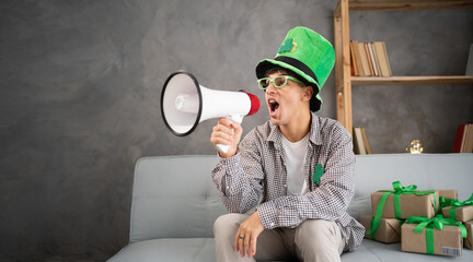 Young smiling man 20s wear leprechauns green hat hold scream in megaphone announces discounts sale...