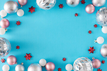 New Year decorations concept. Flat lay holiday composition of pink silver christmas baubles and red stars on pastel blue background with copy space in the middle.