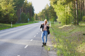 A beautiful blonde girl stands by the road in the forest on a spring day.