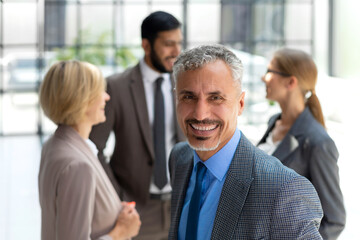 Smiling businessman with colleagues in the background in office.