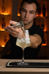 Male bartender pouring alcohol from jigger to glass with ice