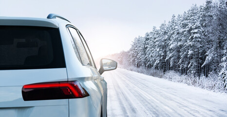 White car on a winter road through a snow covered forest.	