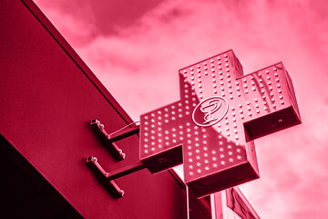 Viva Meganta toned red magenta neon medical bright shining glowing illuminated urban pharmacy drug store cross sign light bulbs outside. Trendy color of the year 2023. Fashion color pattern


