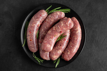 Raw sausages or bratwurst with spices and rosemary in a plate on black background. Top view