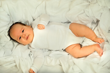 Fototapeta na wymiar newborn baby smiles and laughs. shows emotions. baby lies on a white cloth