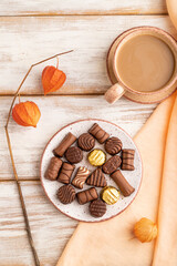 Chocolate candies with cup of coffee and physalis flowers on a white wooden background. top view, close up.