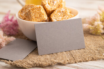 Gray business card with traditional turkish delight (rahat lokum) on a white wooden background. side view, close up.