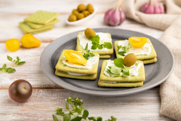 Green cracker sandwiches with cream cheese and cherry tomatoes on white wooden background. side view, selective focus.