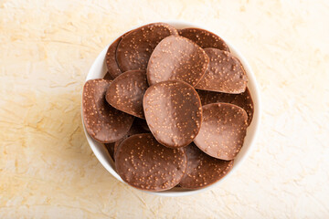Chocolate chips on a beige concrete background. top view, close up.