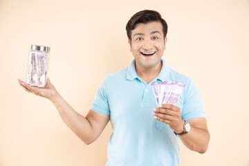 Amazed or cheerful handsome man with Indian rupee notes in one hand and glass jar with lots of cash...