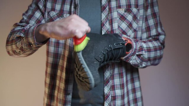 Topic care and brushing warm shoes expertly with small brush in workshop. Professional cleaning of nubuck shoes, suede autumn boots black, winter care and cleaning footwear. Boot maintenance studio. 