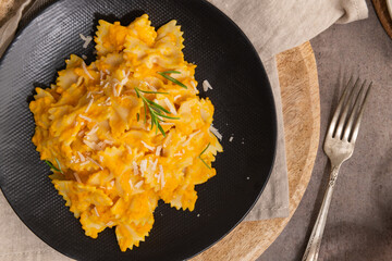 Farfalle pasta with pumpkin sauce and parmesan cheese decorated with rosemary on a black ceramic plate. Creamy cheesy vegan pumpkin pasta. Kitchen counter top. Top view. Flat lay