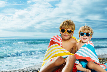 Portrait of two little boys covered in beach towel over sea