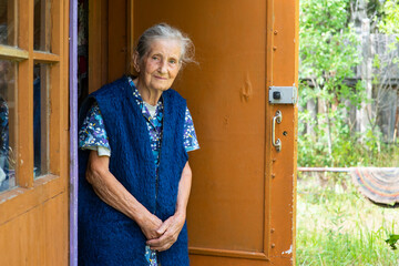 Portrait of an old peasant woman standing in front of a village house.