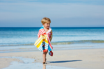 Cute blond boy in towel run after swim on sea sand beach