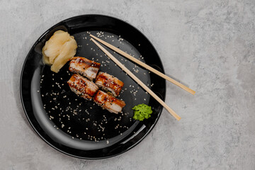 Four portions of shrimp and eel sushi with vossabi sauce and ginger on a black plate.Side view
