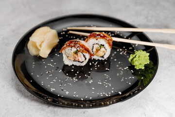 Two servings of shrimp and eel sushi with vossabi sauce and ginger on a black plate