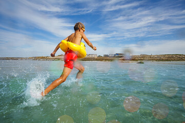 Happy boy run with inflatable duck in sea at the beach