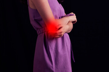 young woman experiencing pain in elbow joint on black background.
