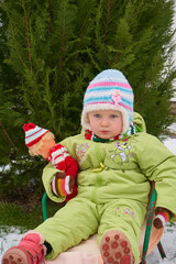 a little girl sits in a sled,portrait of a child with a doll outdoors in winter