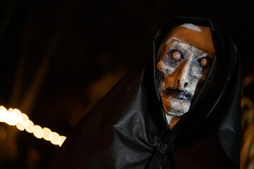 Scary Halloween witch with red eyes in a black cloak in a gloomy environment