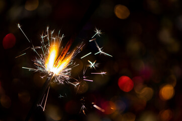 Bright glittering burning sparkler on blurred bokeh background
