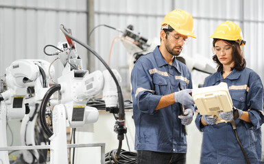 Male industrial engineer using remote control board to check robotic welder operation in modern...