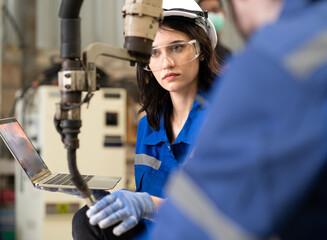 Industrial engineer woman working on robot arm maintenance in modern technology factory. Technician checking robotic automated welding torch machine to control welding process.Innovative engineering.