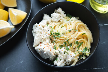 Spaghetti with ricotta cheese, lemon zest and chopped greens served in a black bowl, middle closeup, horizontal shot