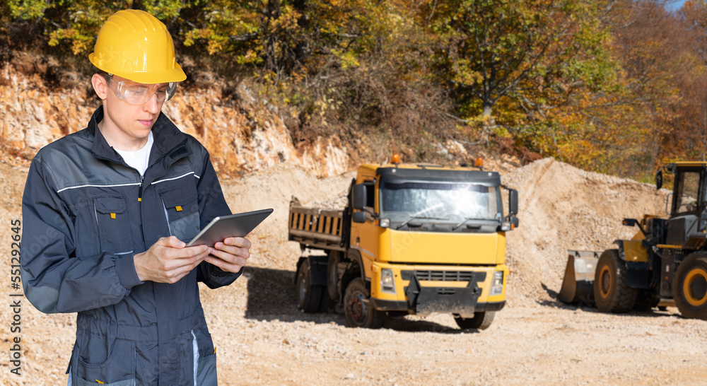 Poster engineer in a helmet with a digital tablet on the background of construction truck