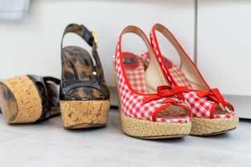 Red and Black pair of open shoes with a high wedge heel in front of a closet