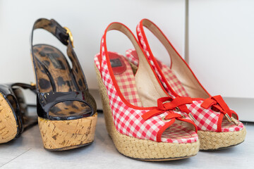 Red and Black pair of open shoes with a high wedge heel in front of a closet