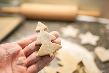 hand holding a christmas-tree shaped christmas cookie cut out of gingerbread dough.