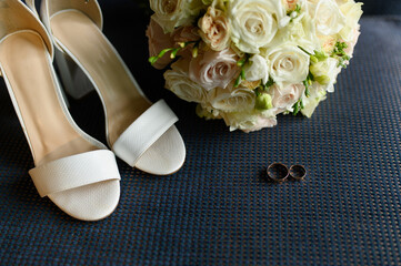 Two stylish wedding rings,a bride's bouquet of roses, sandals on a blue background.Luxurious marriage and love concept