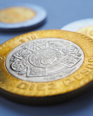 Mexican coins lie on blue surface. Coin of 10 ten pesos close-up. Peso of Mexico. News about economy or banking. Loan and credit. Wages and money. Vertical stories. Macro - obrazy, fototapety, plakaty