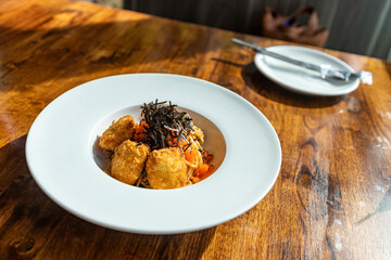 Fusion spaghetti topped with ebiko and seaweed Attached with fried breaded meat. in a white round plate on a wooden table There was sunlight shining through the window. Selective focus.