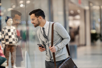 A smart casual trendy businessman is looking at show window in shopping mall.