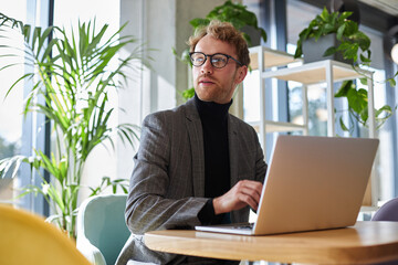 Portrait of young attractive businessman wearing stylish eyeglasses and suit using laptop computer...