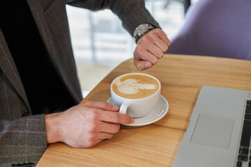 Closeup of businessman hand holding cup of coffee, checking time looking at watch sitting in cafe, selective focus 