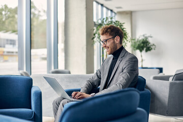 Attractive smiling businessman wearing stylish suit using laptop computer working online planning...