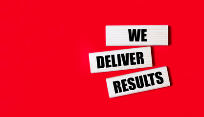 Three wooden blocks with the text WE DELIVER RESULTS on a bright red background. Copy space