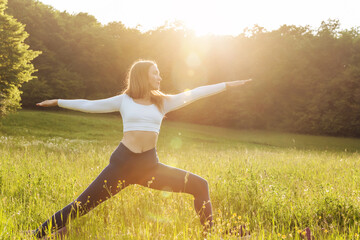 Young woman in sporty outfit exercising and stretching in sunset meadow outdoors. Healthy active lifestyle