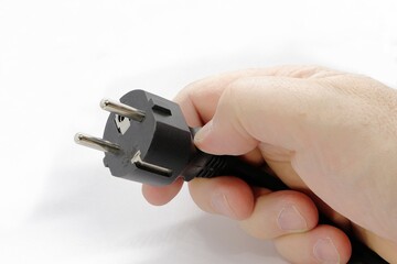 A hand holds an electric plug. Isolated on white background. Power supply cable. - obrazy, fototapety, plakaty