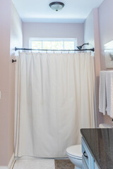 A light pink blush painted guest bathroom shower with the shower curtain closed and a window with...