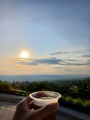 Enjoying coffee in plastic glass in the morning on the  hill with beautiful landscape. Palm hand holding a glass of coffee.