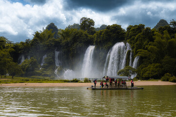 Tourist visiting Ban Gioc Waterfall or Detian Falls by Bamboo boat. Summertime, dramatic sky