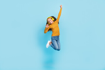 Full size photo of active cheerful person jumping raise fist enjoy new song isolated on blue color background