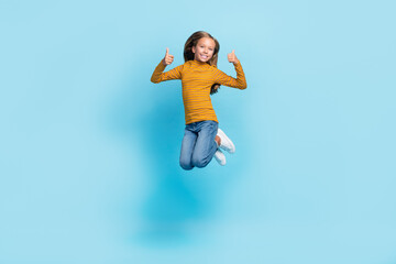 Obraz premium Full body portrait of cheerful girl jumping demonstrate thumbs up feedback isolated on blue color background