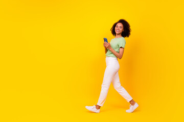 Fototapeta na wymiar Full length photo of young adorable pretty nice woman wear stylish casual outfit phone user addicted positive good mood smiling walk isolated on yellow color background